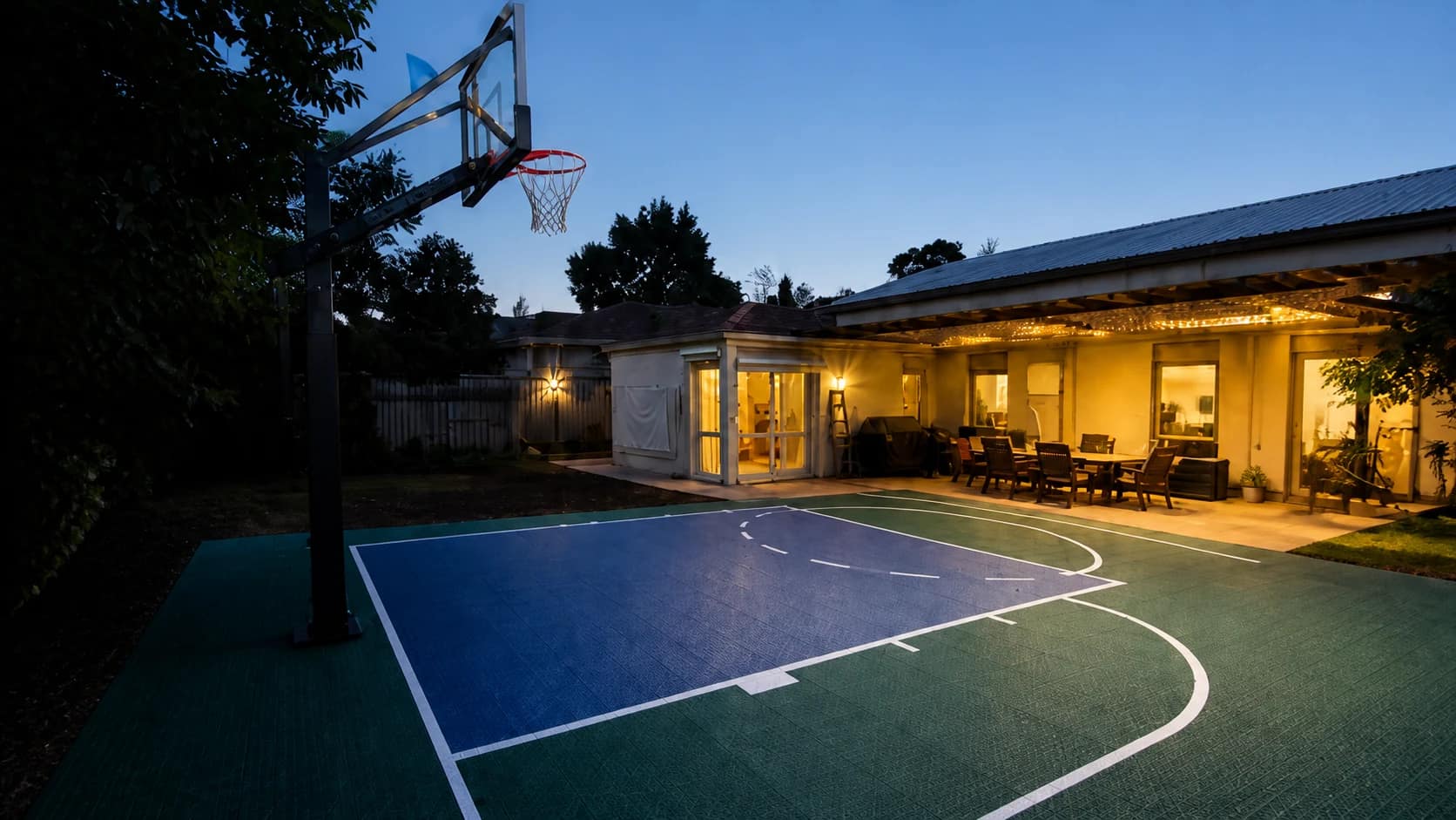 Outdoor modular basketball court beside a home at sunset
