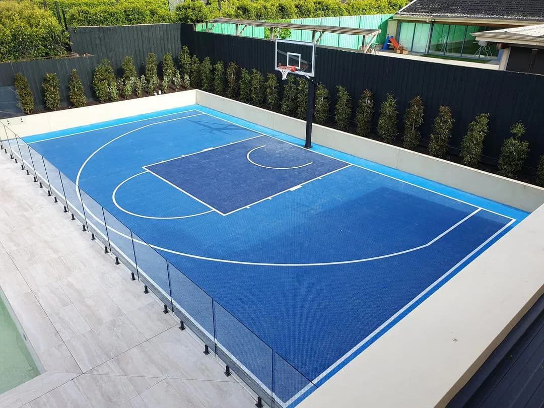 Blue modular basketball court built into a landscaped residential backyard.